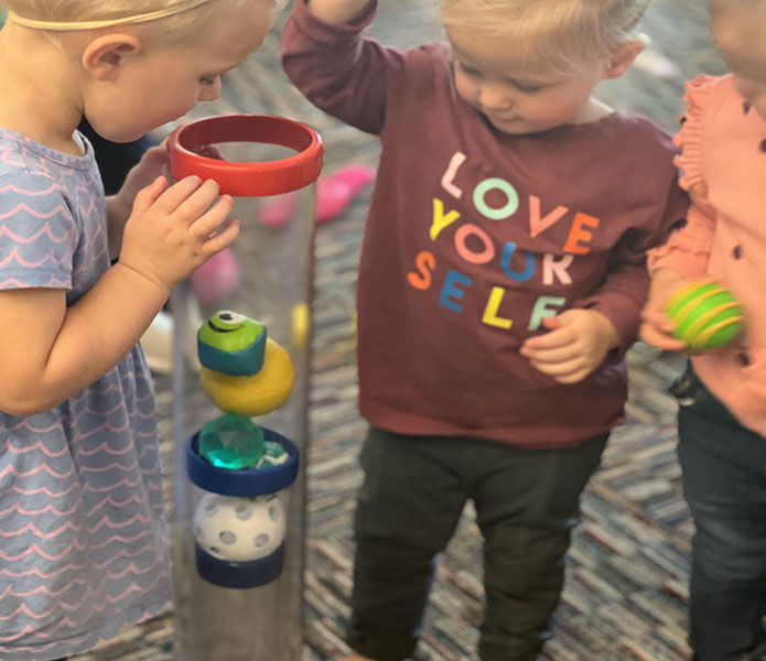 toddlers looking at a tube full of balls