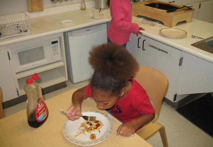 A girl in a red shirt enjoying a pancake.