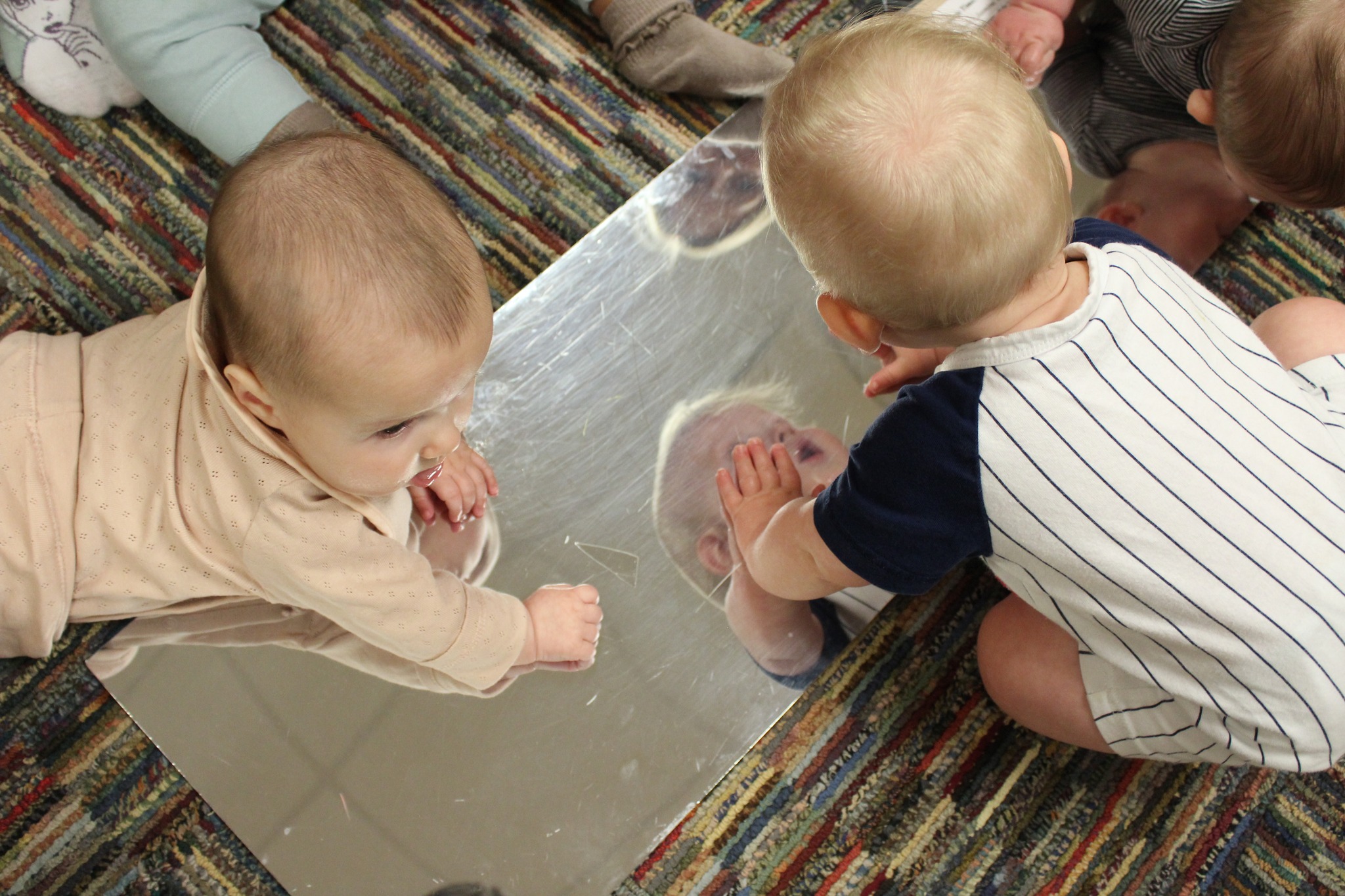 Infants looking at themselves in a mirror on the floor