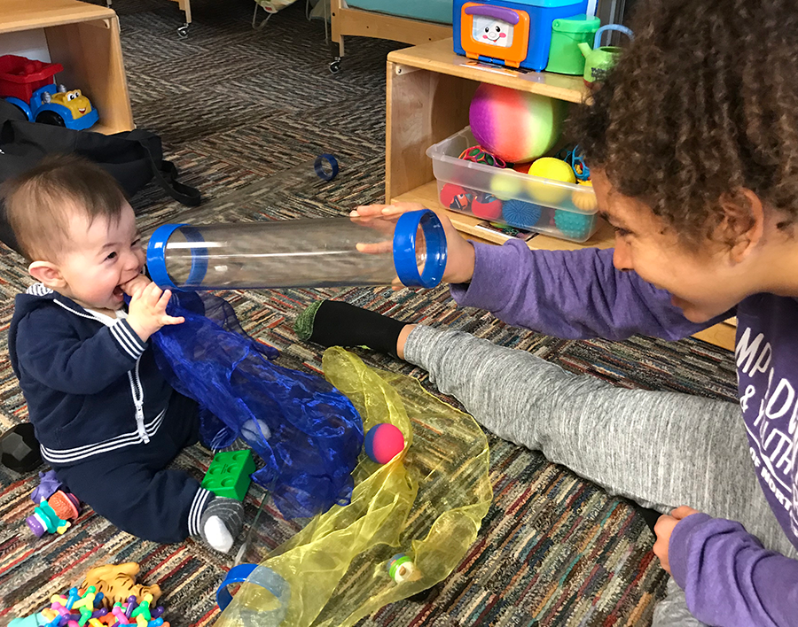 Girl holding a clear tube in front of an infant's face