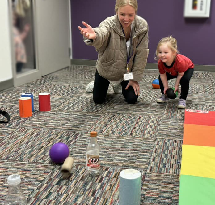 Student showing a young child how to roll a ball