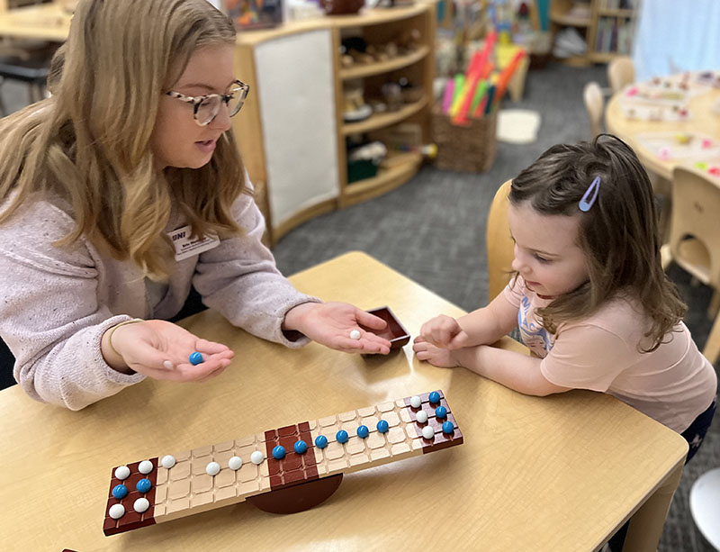 Student showing two different colored marbles to a young child