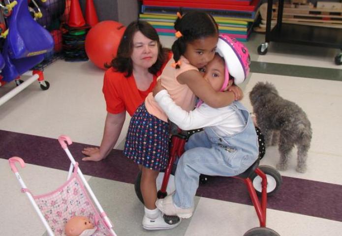 Two young children hugging with teacher looking on