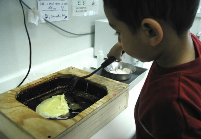 Child cooking an egg in a skillet