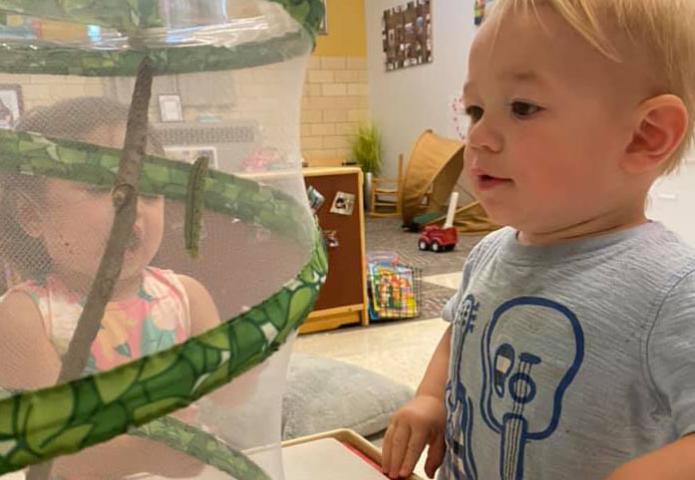 Toddler looking a caterpillar through mesh container