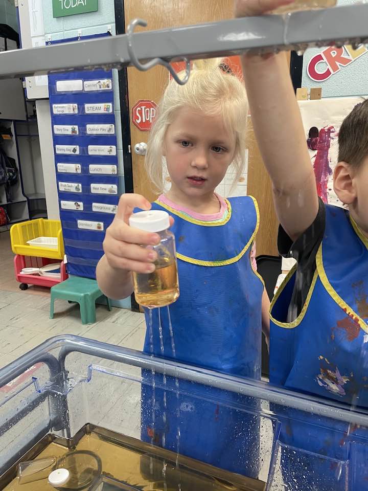 Young girl watches water come out of a bottle with holes