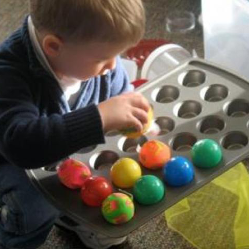 Toddler putting various balls into a muffin tin