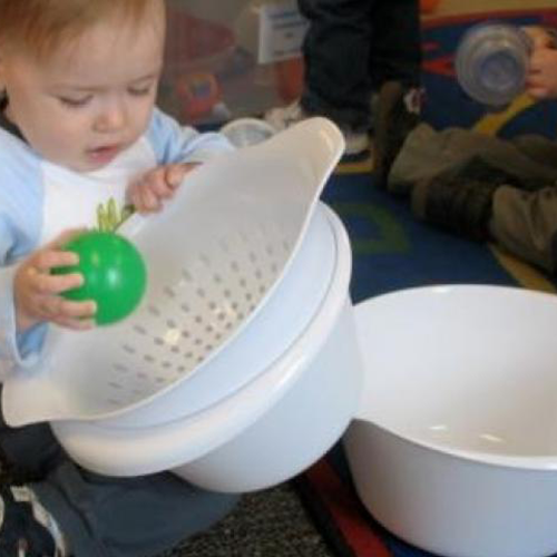 Toddler putting a ball into a colander