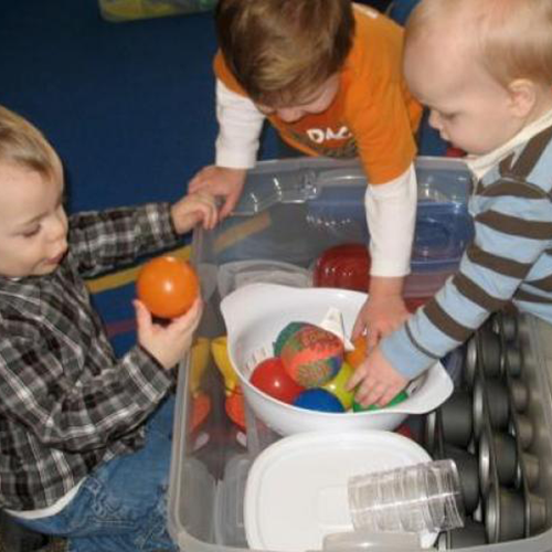 Toddlers grabbing balls from a colander