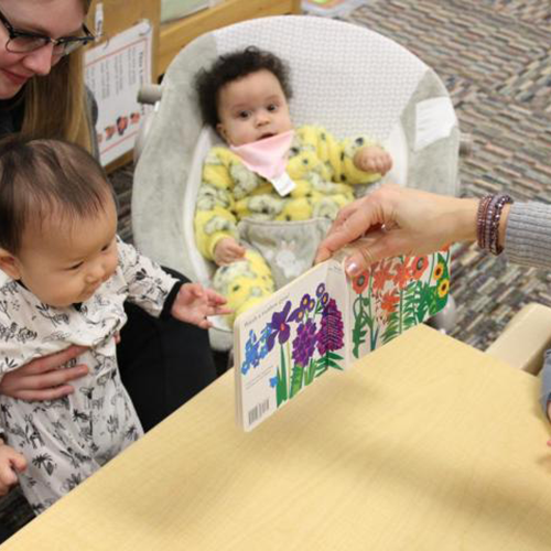 infant looking at a book that is being held by a teacher