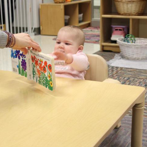 infant looking at a book that is being held by a teacher