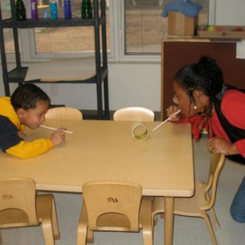 Child and teacher blowing a roll of tape through straws